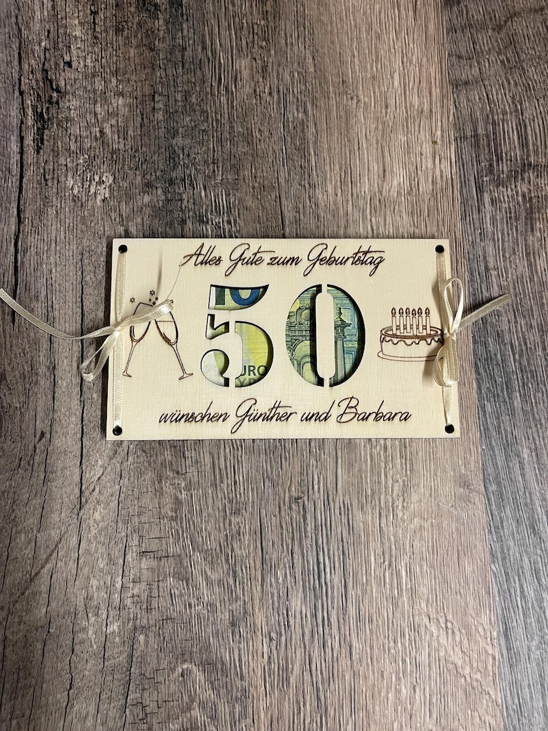 May include: A wooden birthday card with the number 50 cut out, filled with currency. The card has champagne glasses, a cake with candles, and the text "Alles Gute zum Geburtstag w&uuml;nschen G&uuml;nther und Barbara" in a decorative font.