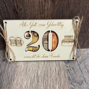 May include: A wooden birthday card with the number 20 cut out, filled with currency. The card includes the text "Alles Gute zum Geburtstag" and "w&uuml;nscht dir deine Familie..." along with illustrations of beer mugs and a cake.