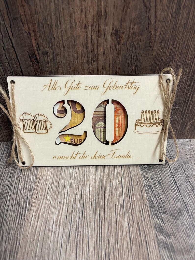 May include: A wooden birthday card with the number 20 cut out, filled with currency. The card includes the text "Alles Gute zum Geburtstag" and "w&uuml;nscht dir deine Familie..." along with illustrations of beer mugs and a cake.