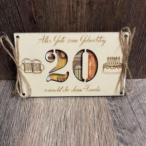 May include: A wooden birthday sign with the number 20 cut out, filled with Euro banknotes. The sign includes laser-cut images of beer mugs and a cake with candles. The text "Alles Gute zum Geburtstag" is engraved on the sign.