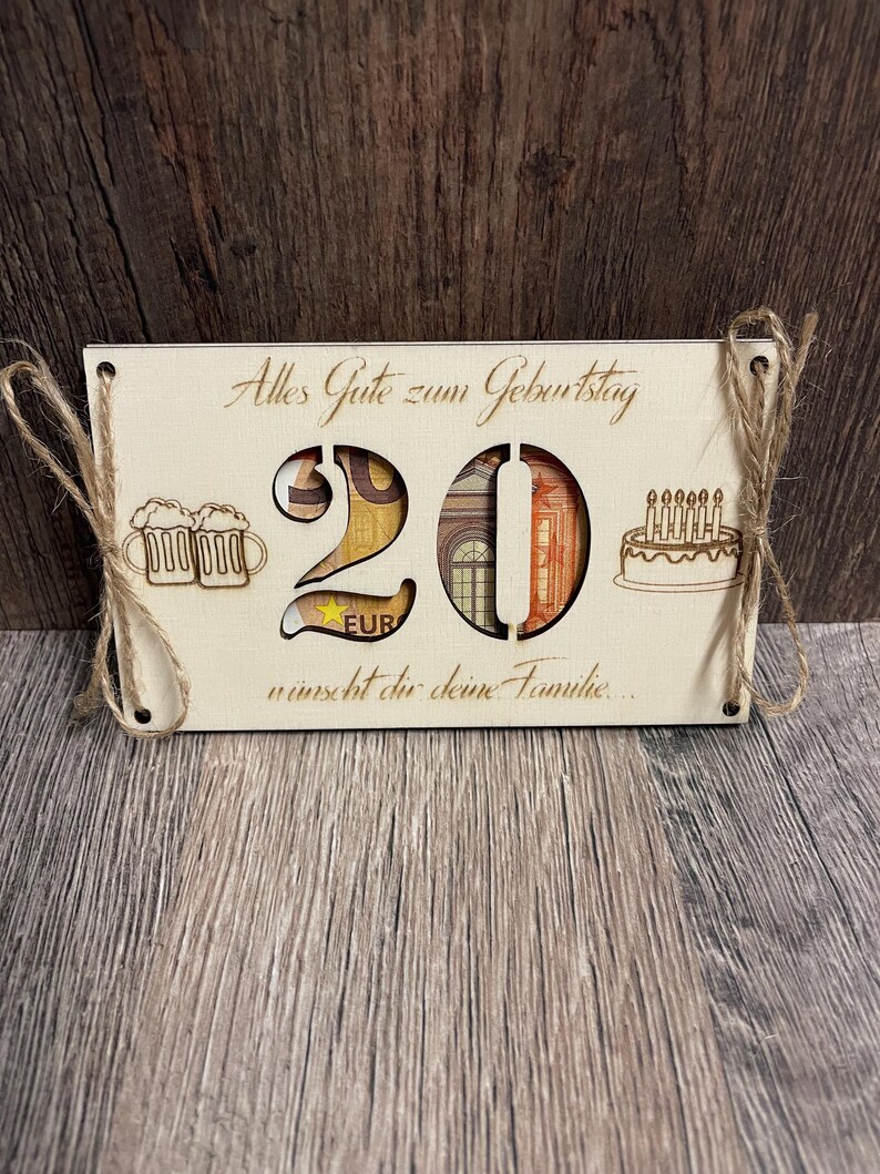May include: A wooden birthday sign with the number 20 cut out, filled with Euro banknotes. The sign includes laser-cut images of beer mugs and a cake with candles. The text "Alles Gute zum Geburtstag" is engraved on the sign.