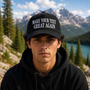K&ouml;nnte beinhalten: Schwarze Baseballkappe mit dem wei&szlig;en Text "MAKE YOUR TEXT GREAT AGAIN". Die Kappe wird von einer Person getragen, die einen schwarzen Kapuzenpullover tr&auml;gt. Der Hintergrund zeigt eine Bergkette und einen See.