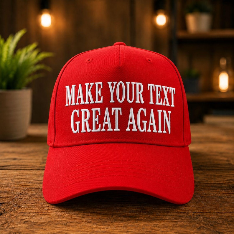 K&ouml;nnte beinhalten: Eine leuchtend rote Baseballkappe mit dem wei&szlig;en, gestickten Text: "MAKE YOUR TEXT GREAT AGAIN". Die Kappe hat einen gebogenen Schirm und besteht aus strapazierf&auml;higem Material. Sie wird auf einer Holzoberfl&auml;che gezeigt.