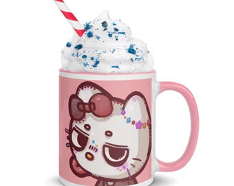 Può includere: Una tazza in ceramica rosa con un manico bianco. La tazza ha uno sfondo rosa e un'immagine di un gatto bianco con occhi blu e un fiocco rosa. Il gatto ha un bastoncino di zucchero rosa e bianco in bocca. La tazza è piena di panna montata bianca e spruzzi blu.