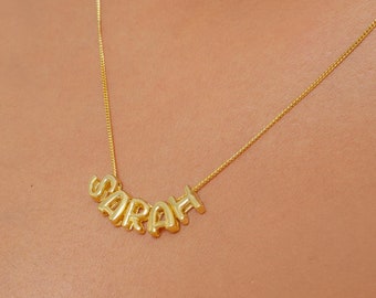 May include: A gold necklace with the name "SARAH" spelled out in cursive letters.