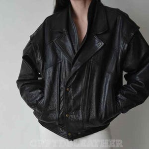Peut inclure: Veste en cuir noir au design classique. Elle présente un col cranté, des fermetures à boutons et des poches. La veste a une coupe légèrement oversize et un aspect texturé. Le nom de la marque "CRFTDSLEATHER" est visible en bas.