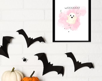 May include: A framed print with a white background and a pink watercolour ghost with the text "wooooo!" in black. The print is surrounded by black bats and pumpkins on a white brick wall.