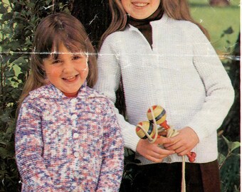 May include: Two girls wearing knitted cardigans. The girl on the left is wearing a multi-colored cardigan with a button closure. The girl on the right is wearing a white cardigan with a zipper closure. Both girls are smiling.