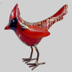 May include: A handcrafted metal cardinal sculpture. The bird features a vibrant red body with black accents on the face and a decorative pattern on the wings. The sculpture stands on thin metal legs.