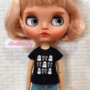 Op de afbeelding: Een zwart T-shirt met een wit spook- en roze strikpatroon. Het shirt is ontworpen voor een pop.