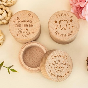 Puede incluir: Cajas de madera para el hada de los dientes con nombres y diseños grabados. Una caja está abierta, revelando el interior. Las tapas presentan nombres como "Brown's", "Ethan's" y "Connor's", junto con ilustraciones de dientes y hadas.
