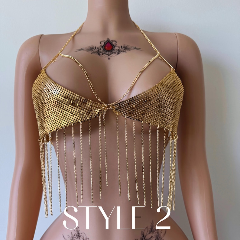 May include: A gold-colored chainmail top with a halter neck and dangling chain fringe. The text "STYLE 2" is displayed in white at the bottom of the image. The top is designed to be worn as a garment.