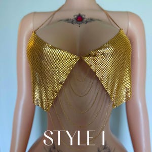 May include: A gold mesh top with a halter neck design and dangling chain details. The top is displayed on a mannequin. The text "STYLE 1" is visible at the bottom of the image.