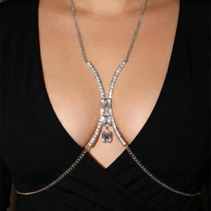Peut inclure: Un collier de corps argent&eacute; orn&eacute; de cristaux transparents &eacute;tincelants. Le collier pr&eacute;sente une cha&icirc;ne d&eacute;licate qui se drape sur la poitrine, avec un motif central de cristaux plus grands. Le design est sym&eacute;trique et &eacute;l&eacute;gant.