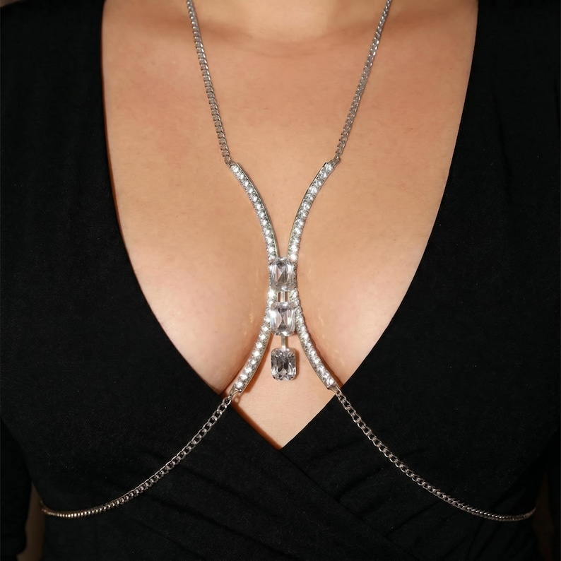 Peut inclure: Un collier de corps argent&eacute; orn&eacute; de cristaux transparents &eacute;tincelants. Le collier pr&eacute;sente une cha&icirc;ne d&eacute;licate qui se drape sur la poitrine, avec un motif central de cristaux plus grands. Le design est sym&eacute;trique et &eacute;l&eacute;gant.