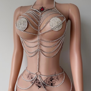 May include: A silver chain body jewelry piece with rhinestones. The chain is layered and has a delicate design. The jewelry is worn on a mannequin.