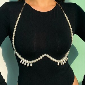 Peut inclure: Un collier de corps en perles avec une fine cha&icirc;ne dor&eacute;e et de fausses perles blanches. Le collier drape sur la poitrine et comporte des pendentifs en perles en forme de goutte.