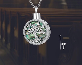May include: A silver-colored pendant necklace with a round, tree-of-life design. The pendant features a detailed tree with iridescent green and blue accents. The necklace includes a small tool, likely for filling the pendant.