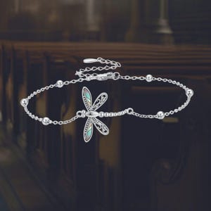 Könnte beinhalten: Ein silbernes Armband mit einem Libellen-Anhänger. Die Libelle hat detaillierte Flügel mit farbigen Akzenten. Die Armbandkette enthält kleine, runde Perlen. Der Verschluss ist am Ende der Kette sichtbar.