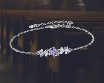May include: Silver bracelet featuring a floral design with purple and clear gemstones. The bracelet has a delicate chain and a central cluster of flowers and leaves. The gemstones are set in a silver metal setting, creating a sparkling and elegant look.