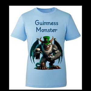 May include: Light blue t-shirt with a graphic of a green-skinned monster wearing a green hat and holding a glass of Guinness. The text "Guinness Monster" is printed on the shirt.