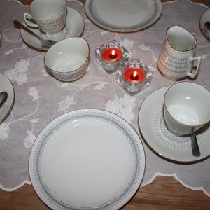 May include: A set of three ceramic mugs with a speckled, matte finish. The mugs are in shades of cream, light gray, and dark gray. Each mug has a simple, minimalist design and a rounded handle. The mugs are likely for coffee or tea.