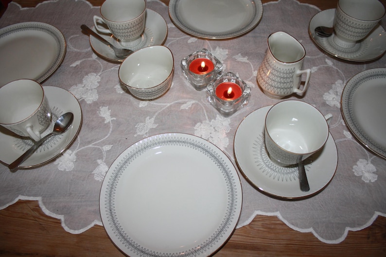 May include: A set of three ceramic mugs with a speckled, matte finish. The mugs are in shades of cream, light gray, and dark gray. Each mug has a simple, minimalist design and a rounded handle. The mugs are likely for coffee or tea.