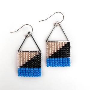 May include: A pair of handmade beaded earrings. Each earring features a silver triangle top and a rectangular beaded section with a color gradient of tan, black, and blue. The earrings hang from silver hooks.