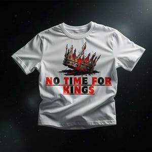 Peut inclure: T-shirt blanc avec un motif de couronne aux accents rouges, dorés et verts. Le texte "NO TIME FOR KINGS" est imprimé en rouge et noir en dessous. Le t-shirt est présenté sur un fond sombre.