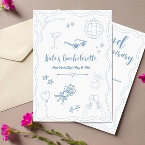 May include: A white card with blue illustrations of a cocktail glass, sunglasses, a disco ball, a ring with a diamond, a rose, and two champagne glasses. The text on the card reads "Kate's Bachelorette New York City| May 9-11th".
