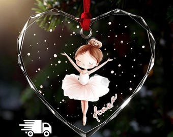 May include: A heart-shaped clear acrylic ornament with faceted edges, featuring a printed illustration of a young ballerina in a white tutu and a bun hairstyle. The name Hana is written in script, and the ornament hangs from a red ribbon.