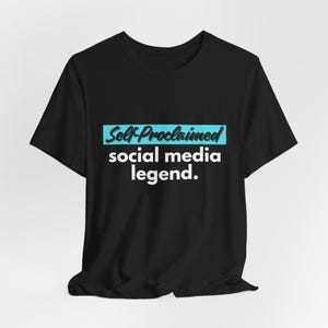 May include: Black t-shirt with the text "Self-Proclaimed social media legend." in white font, with the words "Self-Proclaimed" in a teal rectangle. The shirt is made of a soft material.