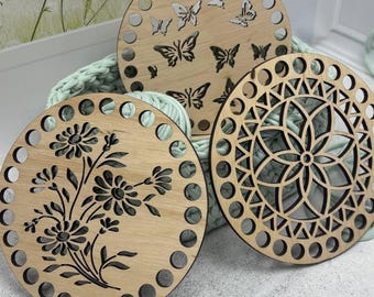 Könnte beinhalten: Drei hölzerne Korbunterseiten mit dekorativen Ausschnitten. Eines zeigt Schmetterlinge, ein anderes ein Blumenmuster und das dritte ein geometrisches Design. Jede Basis hat eine Reihe von gleichmäßig verteilten Löchern am Umfang, aus hellem Holz.