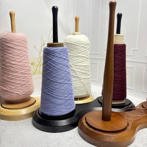 Puede incluir: Soportes de hilo de madera con carretes de hilo en varios colores: rosa, azul, blanco y burdeos. Los soportes tienen una base de madera y un husillo central. El hilo está bien enrollado alrededor de los carretes.