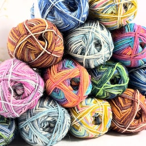 May include: A selection of multi-coloured yarn balls in shades of blue, green, pink, orange, yellow, and brown. The yarn is tightly wound, with visible strands of different colours creating a textured appearance. Suitable for knitting and crochet projects.