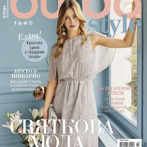 May include: A magazine cover featuring a woman in a light gray dress with a cape-like overlay. The cover includes the text "BURDA STYLE" and "Extra!" in large fonts. A vase of white flowers is visible.