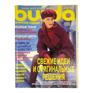Puede incluir: Una portada de la revista Burda vintage con una mujer vestida con un atuendo burdeos, que incluye boina, abrigo y guantes. La portada tiene texto en amarillo y blanco, con el título "Burda" en letras grandes. La revista es de 1997.