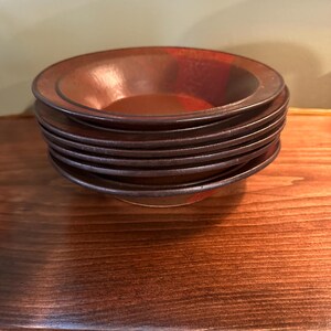 May include: A stack of six brown ceramic bowls with a red glaze. The bowls are stacked on a wooden surface.