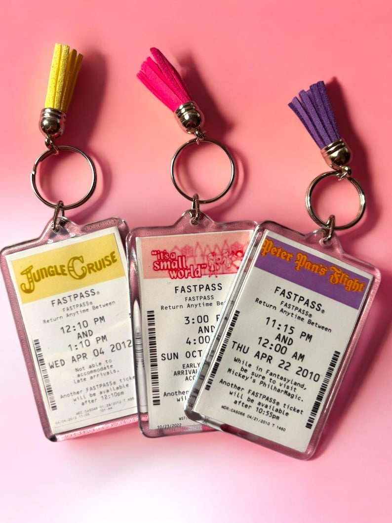 Puede incluir: Tres llaveros rectangulares de acr&iacute;lico con r&eacute;plicas de boletos Fastpass de parques tem&aacute;ticos para Jungle Cruise, It's a Small World y Peter Pan's Flight. Cada llavero incluye una anilla de metal plateado y una borla de ante en amarillo, rosa o morado.