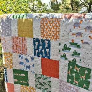 May include: A patchwork quilt with a variety of animal prints, including turtles, cats, giraffes, and walruses. The quilt is made of different colored fabrics, including green, orange, yellow, and blue. The quilt is hanging on a wooden rod.
