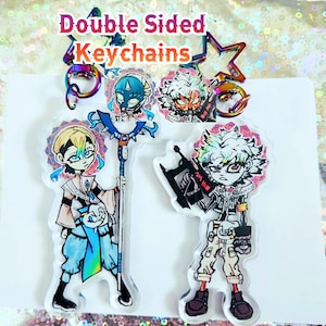 May include: Double-sided keychains featuring anime-style characters. One keychain shows a character with a staff, the other with a weapon. The keychains have iridescent hardware and the text "Double Sided Keychains".