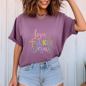 May include: A purple t-shirt with the text "Love Like Jesus" in colorful lettering. The text includes a cross and a peace sign.