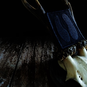 May include: A close-up of a deer antler mount with a dark blue fabric accent. The fabric has a textured design and is attached to the base of the antlers. The antlers are a light brown colour, and the skull is white.