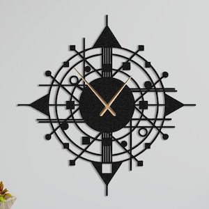 May include: A black, geometric wall clock with gold-colored hands. The clock features a circular design with various shapes and lines, creating a modern, abstract aesthetic. The clock is mounted on a white wall above a wooden cabinet.