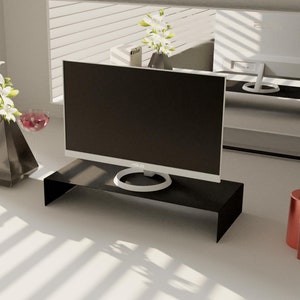 May include: A white desk with a black monitor stand, a black computer monitor, a white vase with white flowers, a clear glass with a red liquid, a white box with the text "keep it simple", a clear glass bottle with a red liquid, and two bottles with red liquid.