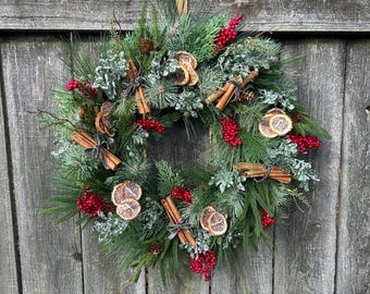 May include: A green Christmas wreath decorated with cinnamon sticks, dried orange slices, and red berries.