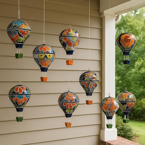 May include: A display of hanging hot air balloon ornaments. Each balloon is adorned with a vibrant floral pattern in shades of orange, blue, and green. The balloons are suspended by wires, with small square baskets below.