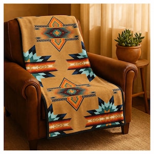 Puede incluir: Una manta de color tostado con un patrón geométrico repetitivo en tonos turquesa, naranja, negro y blanco. La manta está colocada sobre un sillón de cuero marrón, mostrando un diseño simétrico con motivos de estrellas y líneas.