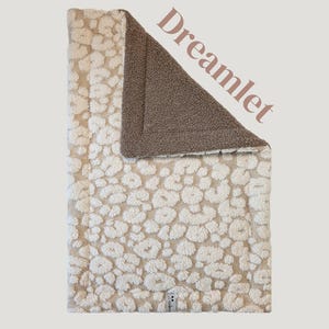 Op de afbeelding: Een omkeerbare deken met een crèmekleurige luipaardprint aan de ene kant en een effen bruine kleur aan de andere kant. De deken heeft een zachte textuur en het woord "Dreamlet" staat op de deken.