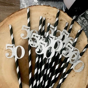 Può includere: Primo piano di un piatto di legno con cannucce a strisce nere e argento. Ogni cannuccia ha un numero 50 di glitter argento attaccato alla parte superiore.
